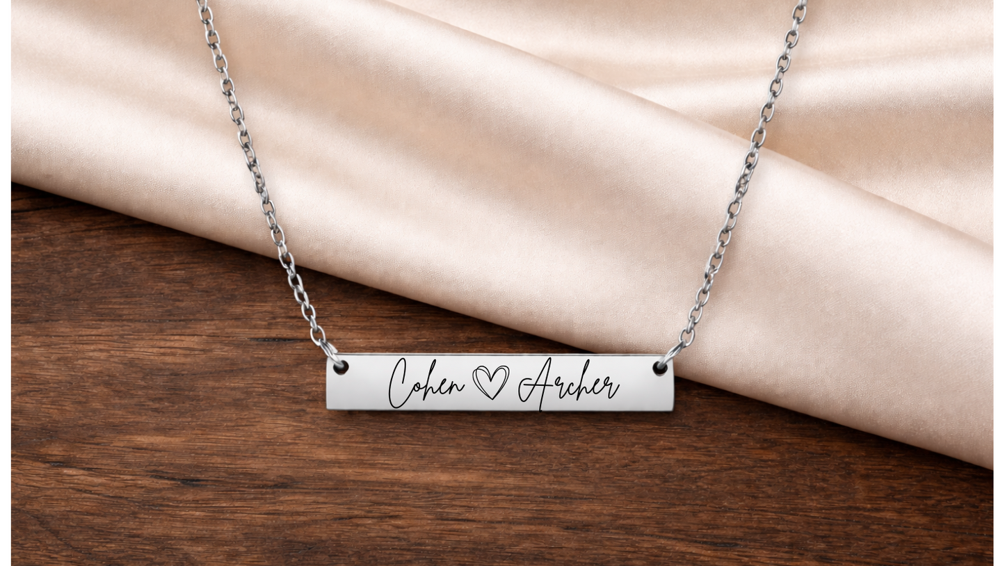 Silver bar necklace with engraved text on a wooden surface